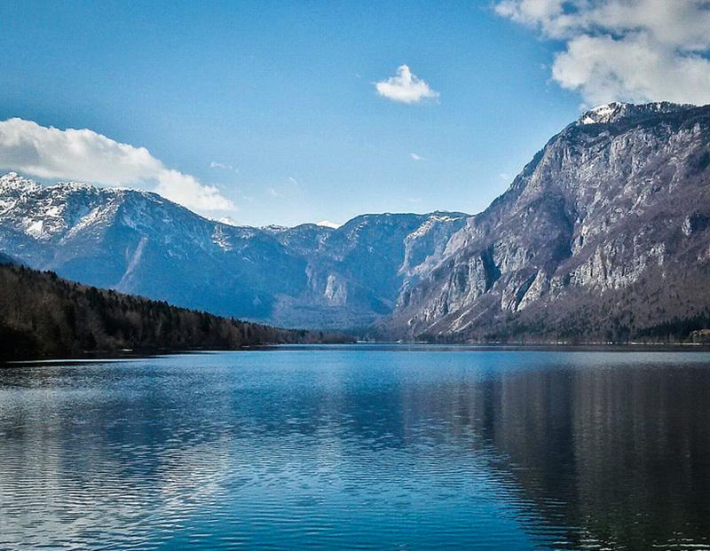 Panoramic view of the serene waters of Lake Bohinj and the steep Julian Alps, promoting Slovenia's natural beauty and the setting for cycling tours.