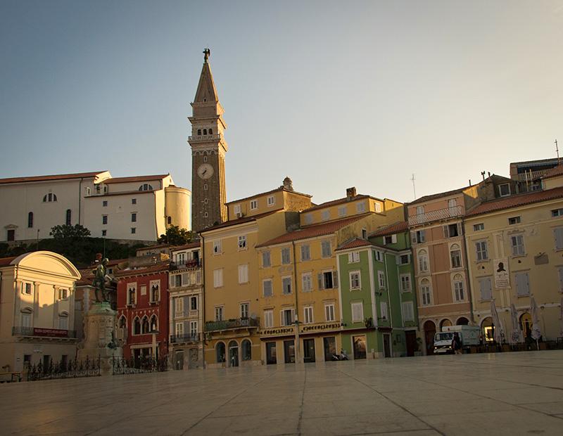 The iconic Tartini Square in Piran, Slovenia, featuring colorful buildings and the tall bell tower. A must-see destination on a self-guided Slovenian coastal cycling itinerary.