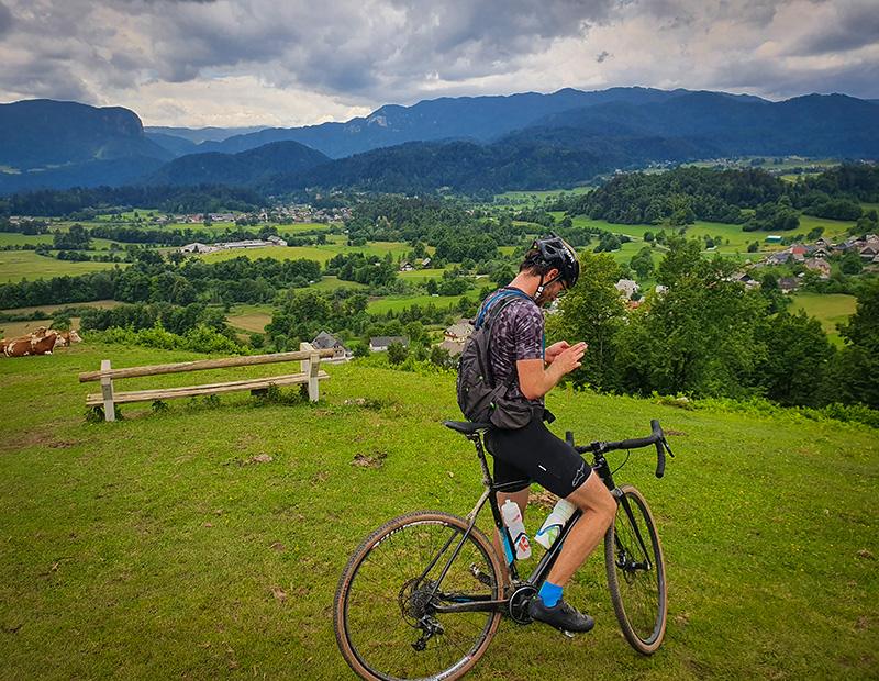 Gravel cyclist checking navigation at a scenic viewpoint overlooking the green valley near Bled, Slovenia. Adventure cycling tour with Helia.