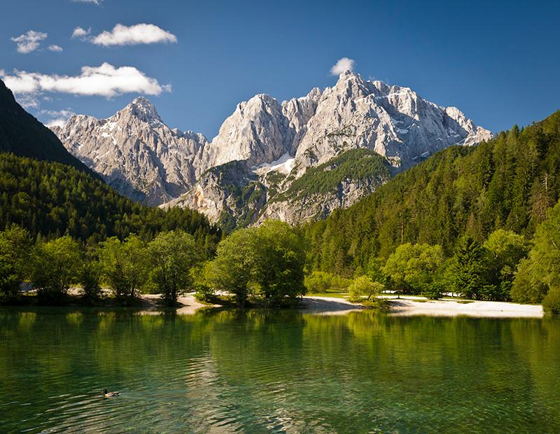 Stunning view of the clear emerald water of Lake Jasna with the majestic, jagged peaks of the Julian Alps towering in the background. A beautiful stop on a Helia cycling route.