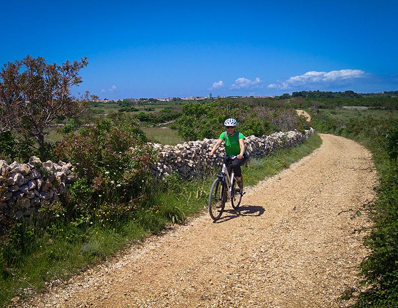 Solo cyclist riding gravel path stone walls Croatian island Mediterranean landscape