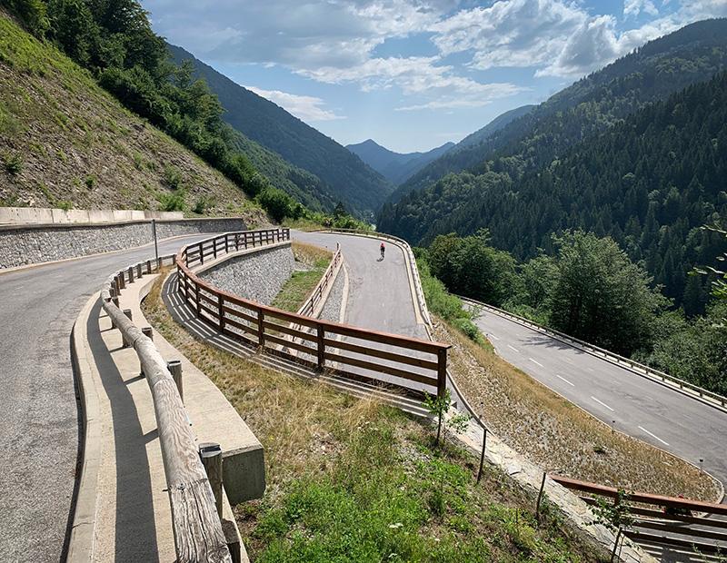 Cyclist climbing a steep mountain switchback road surrounded by dense forests and dramatic alpine valleys in Slovenia.
