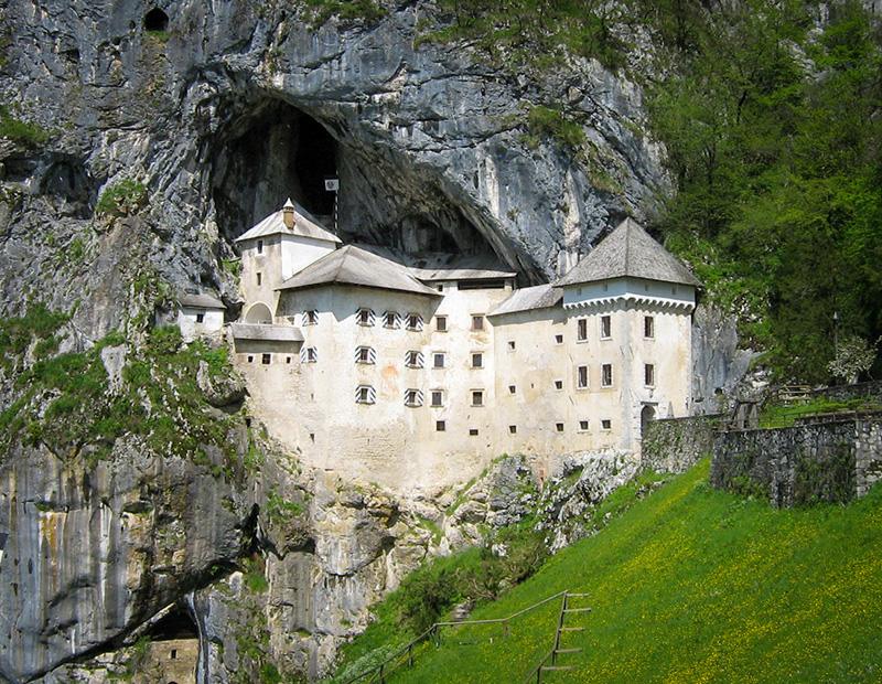 The iconic Predjama Castle built into a cave mouth, a unique historical landmark to visit on a Slovenia tourism cultural or cycling tour.
