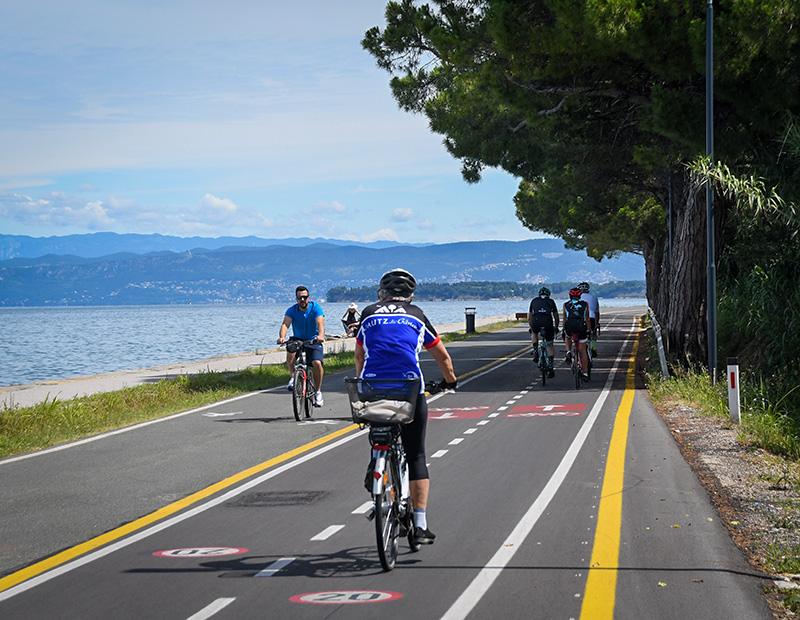 Group of cyclists riding along a dedicated paved bike path next to the sea, promoting safe and enjoyable coastal cycling tours and active Slovenia tourism.